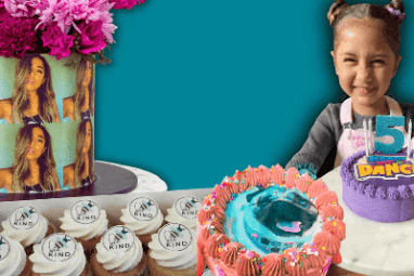 Child with a birthday cake and cupcakes on a table against a teal blue background
